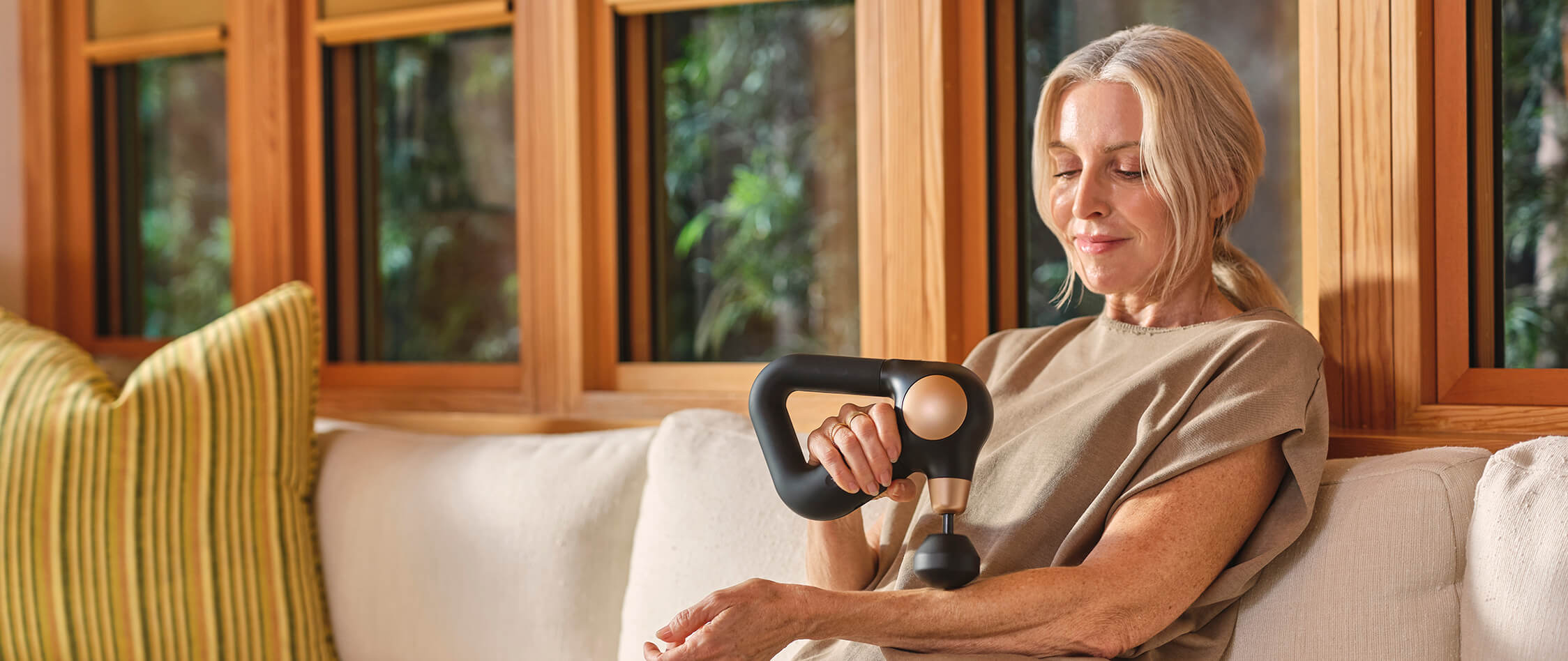 Woman sitting on couch using Theragun Sense 2.0